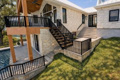 Exterior detail showing black railings, stone walls, wood deck posts, stairs, and the pool area of a Hill Country home.